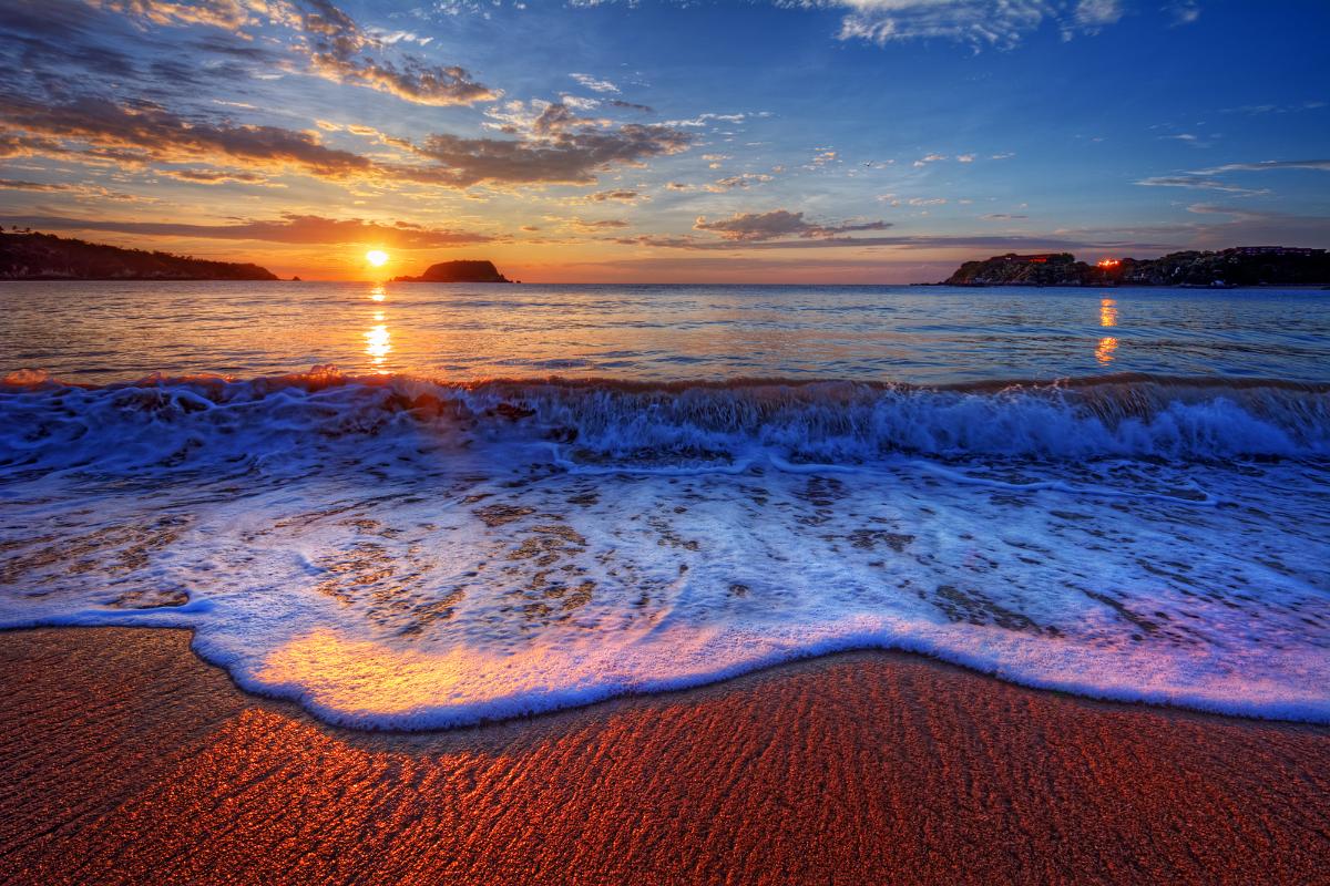 Colorful sunrise over a beach with breaking waves, captured in vivid hues of orange, pink, and blue. This serene coastal landscape represents the calming and therapeutic aspects promoted by Exposure Therapy Designs.